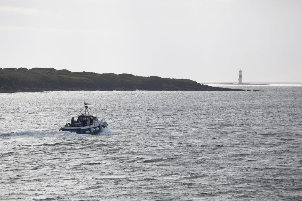 Small tour boat travels across the Atlantic in Sligo Bay, with a lighthouse visible on a distant headland.