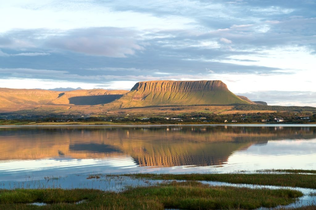 Ben Bulben’s distinctive flat-topped silhouette reflected in calm waters near Drumcliffe, County Sligo, at golden hour.