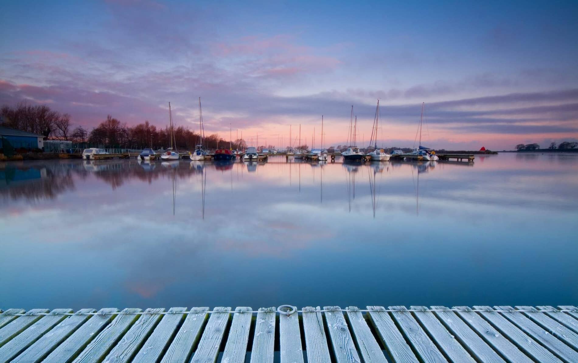 Yachts rest in Lough Neagh at Ballyholme Marina near Bangor at dusk, with pink-tinged skies reflected in the still harbour.