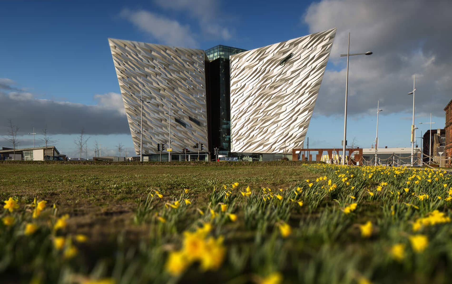 Titanic Belfast’s angular silver facade towers above a bed of daffodils under a bright blue spring sky in Belfast, County Antrim.