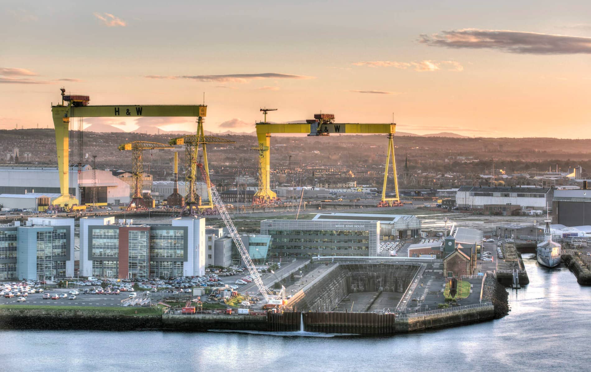 View of the Titanic dry dock and pump house at sunset, with Sampson and Goliath cranes towering above.
