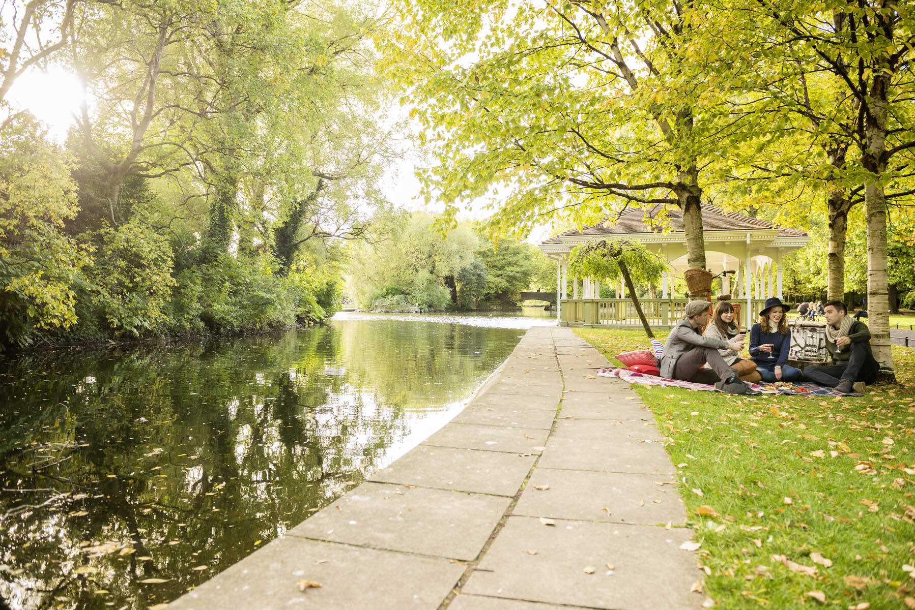 Friends enjoying a picnic under trees beside a pond in Stephen's Green Park, Dublin.