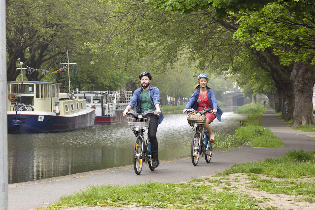 Two people cycling along Dublin’s Grand Canal with moored boats in the background.