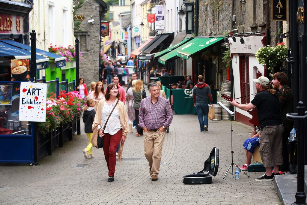 Visitors walking along a lively street with shops and musicians, County Kilkenny.