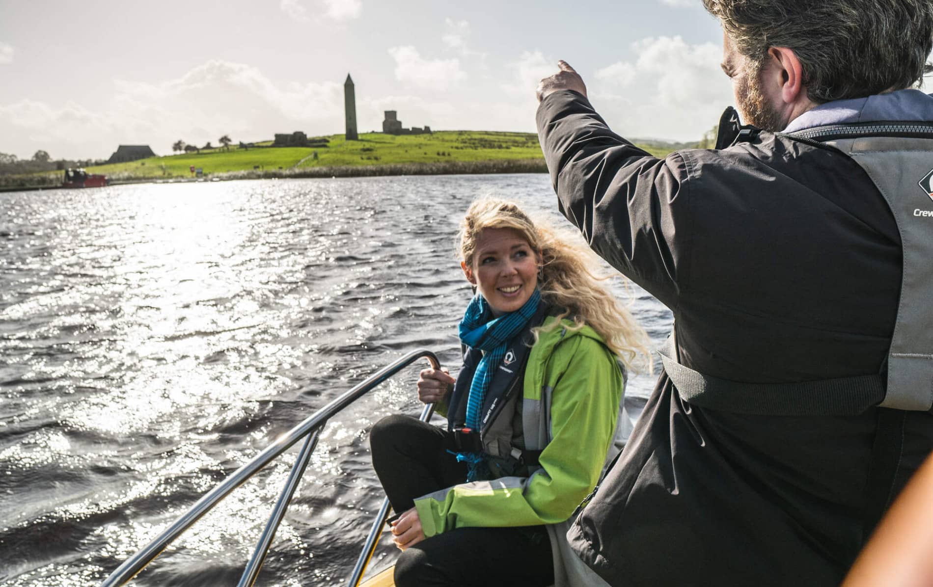 Smiling passenger and guide on a boat taxi across Lough Erne with Devenish Island monastery in the background.