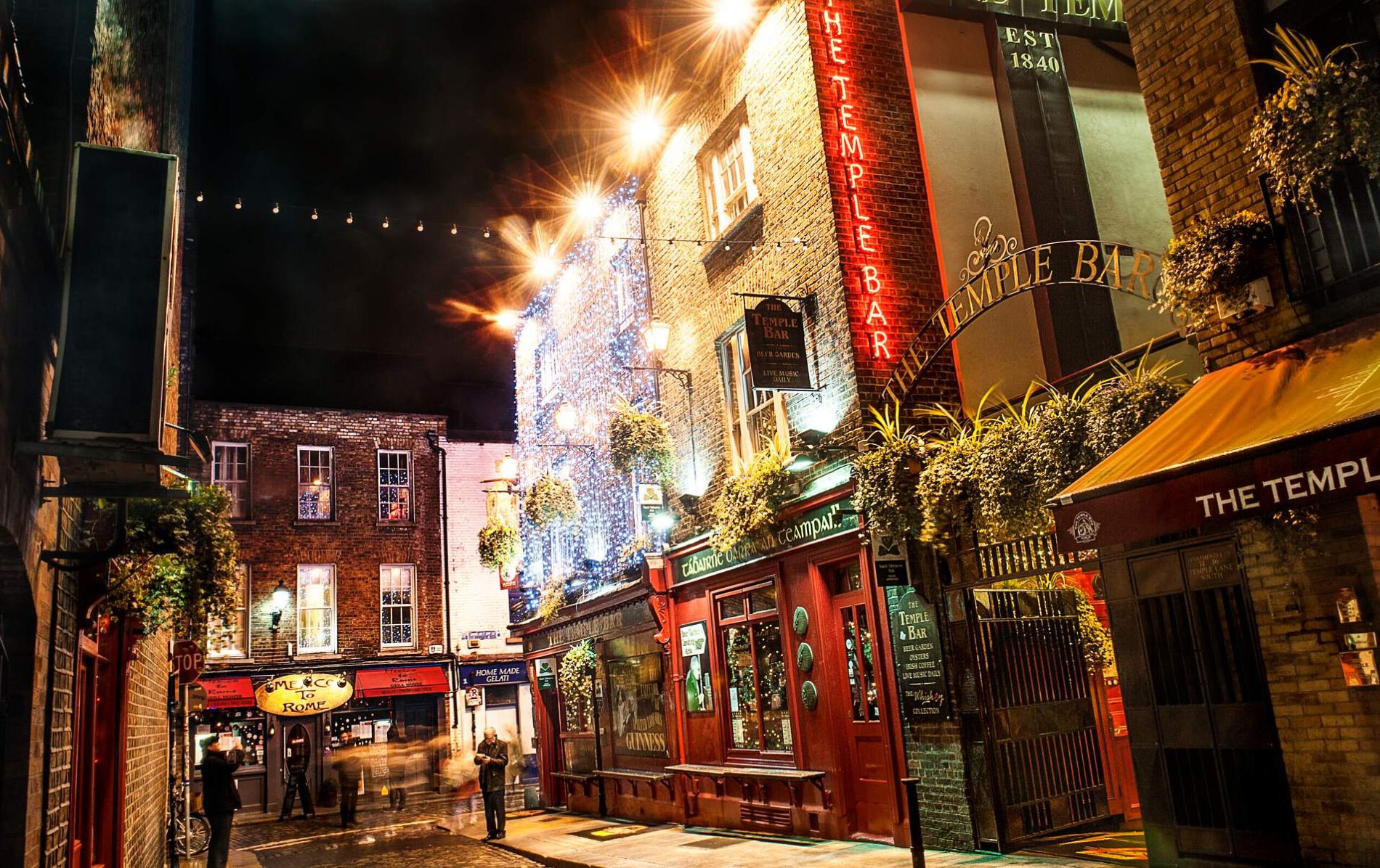Temple Bar street at night with pubs lit by fairy lights and neon signs.