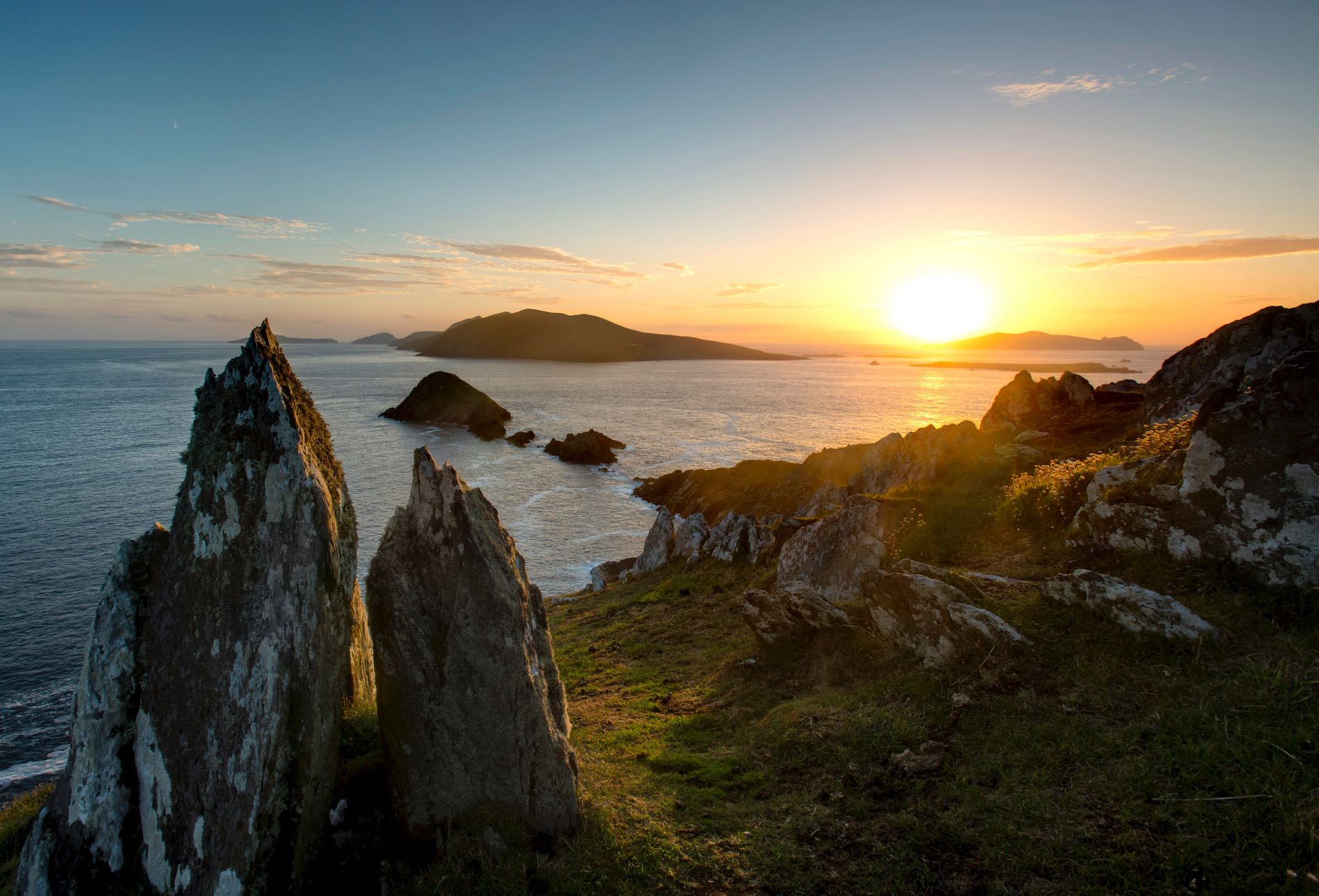 Sunset over the Blasket Islands, viewed from a rocky headland on the Dingle Peninsula, with jagged sea stacks in silhouette.
