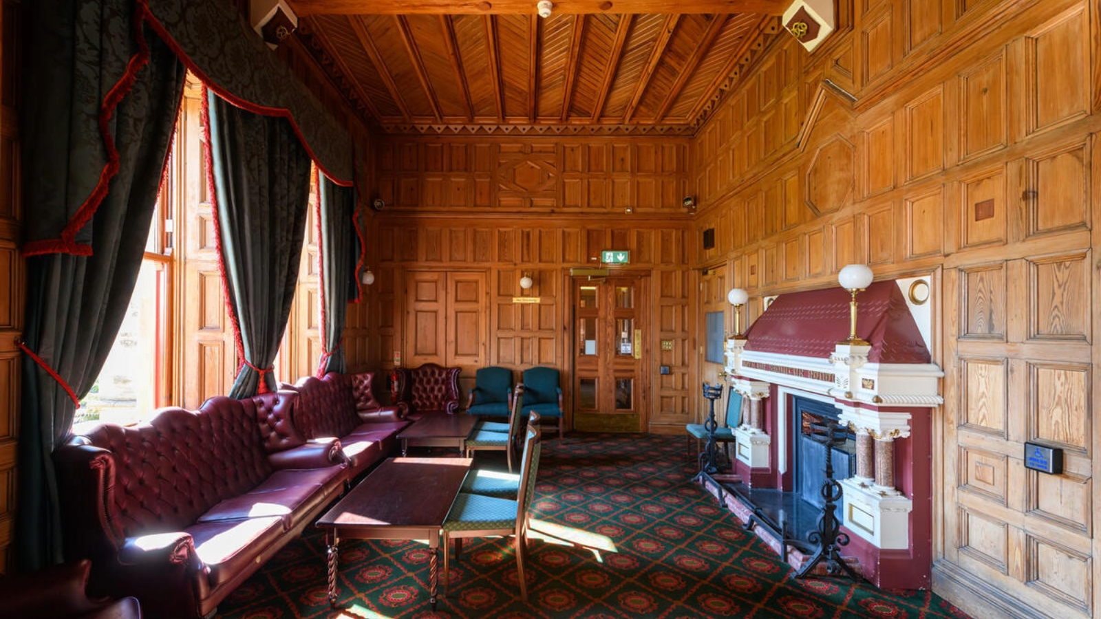 Wood-panelled drawing room at Belfast Castle with ornate fireplace, leather sofas and tall windows overlooking the grounds.