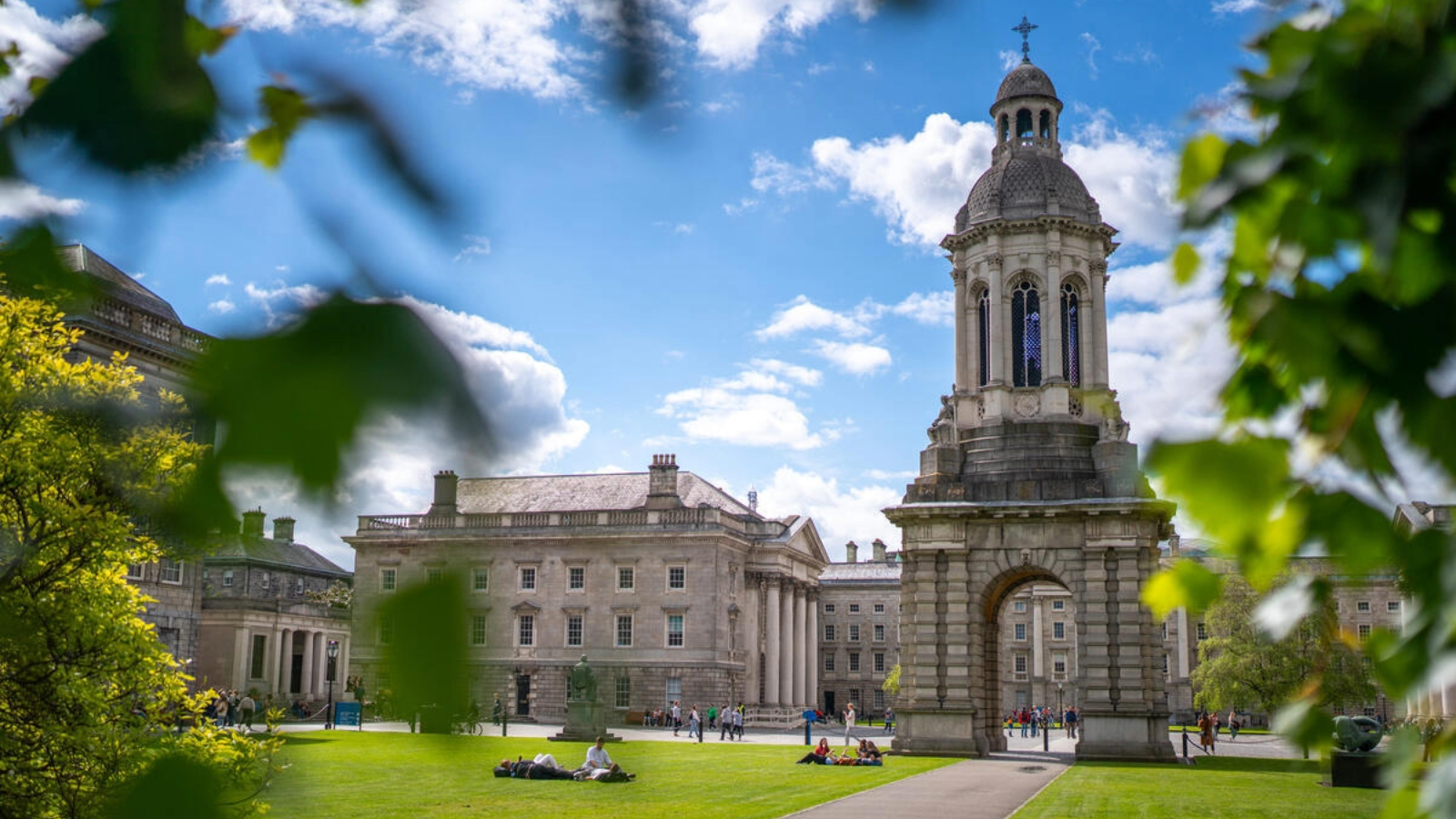 Trinity College Dublin campus view with the Campanile tower framed by green leaves on a sunny day.