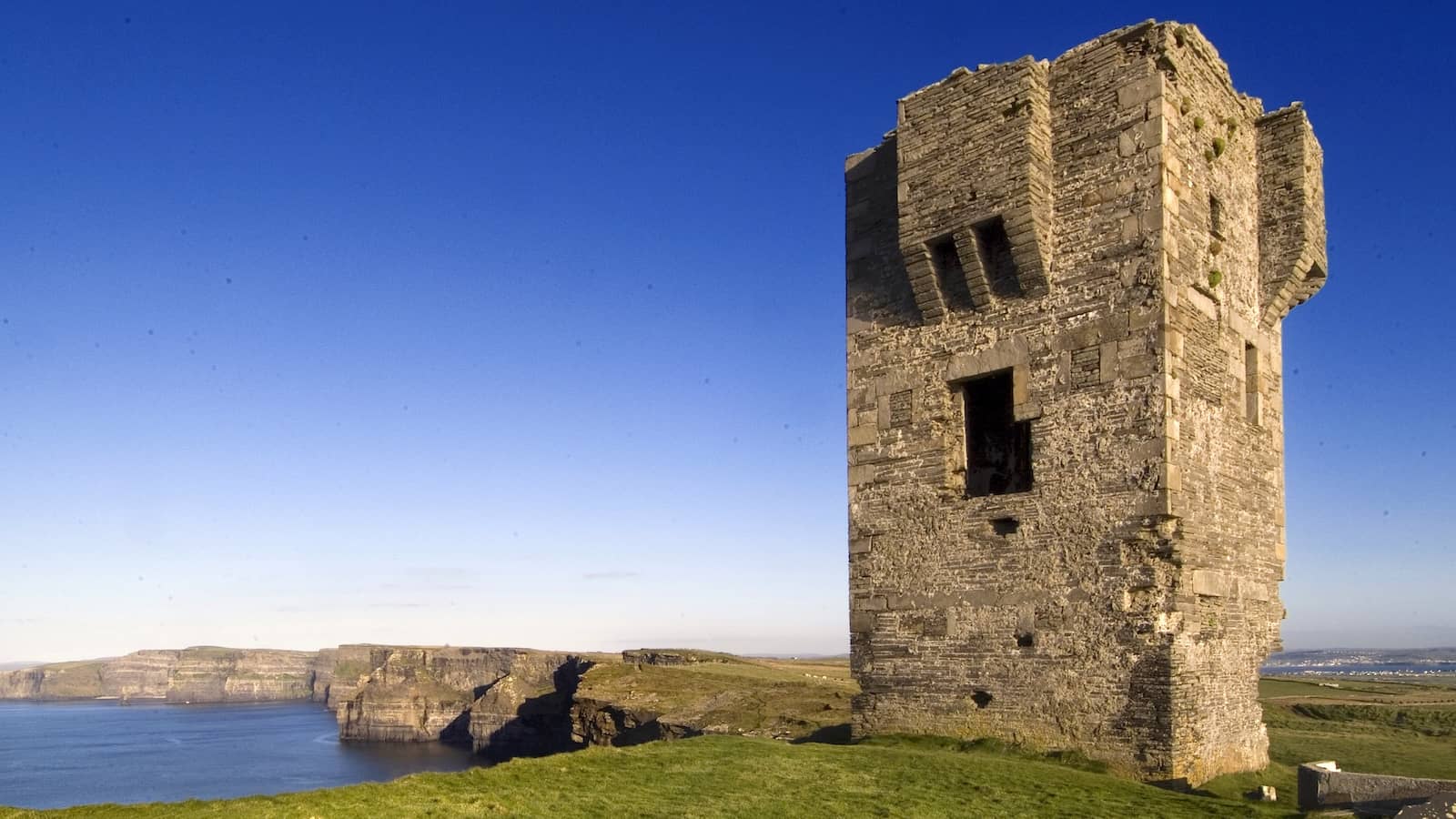 Close view of O’Brien’s Tower standing above the Cliffs of Moher with blue skies and distant coastline.