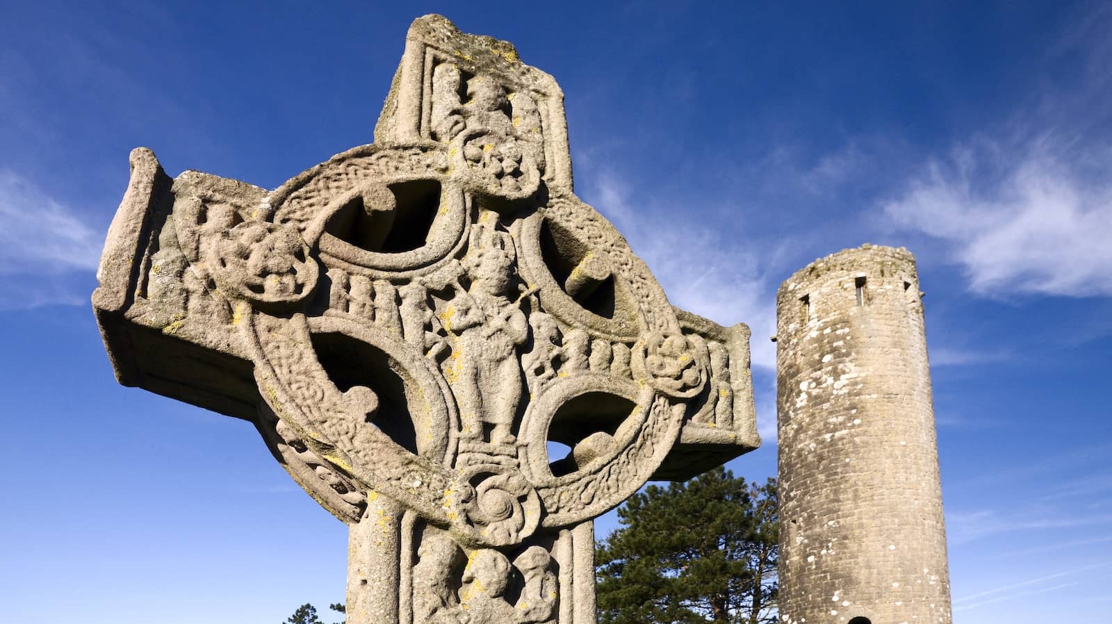 Close-up of a carved high cross at Clonmacnoise with a round tower in the background, County Offaly.