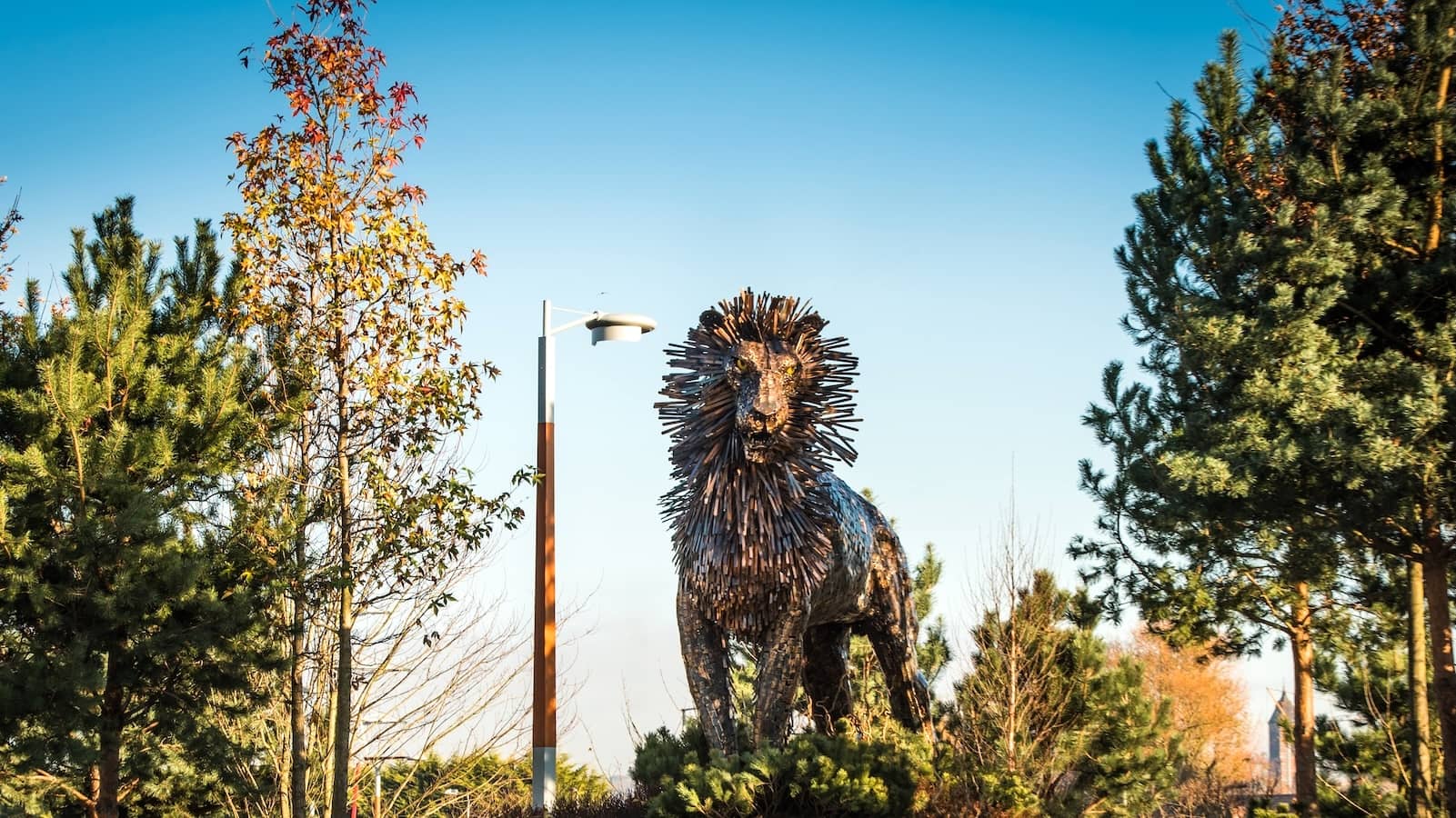 Large metal Aslan lion sculpture among trees at CS Lewis Square in Belfast.