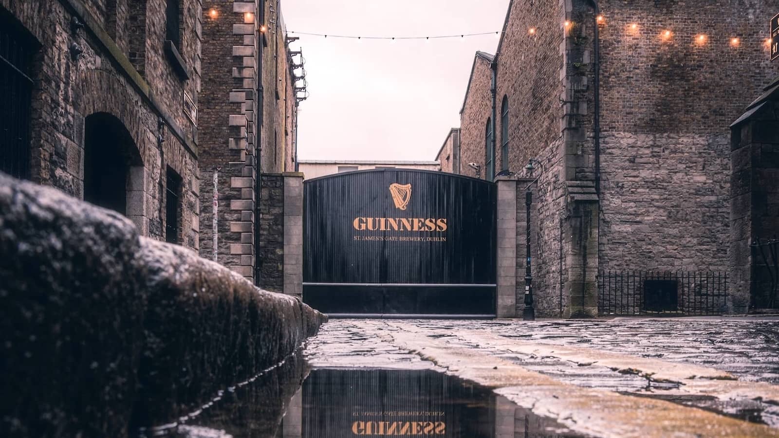 Guinness Storehouse gates at St James’s Gate Brewery in Dublin, with wet cobblestones after rain.