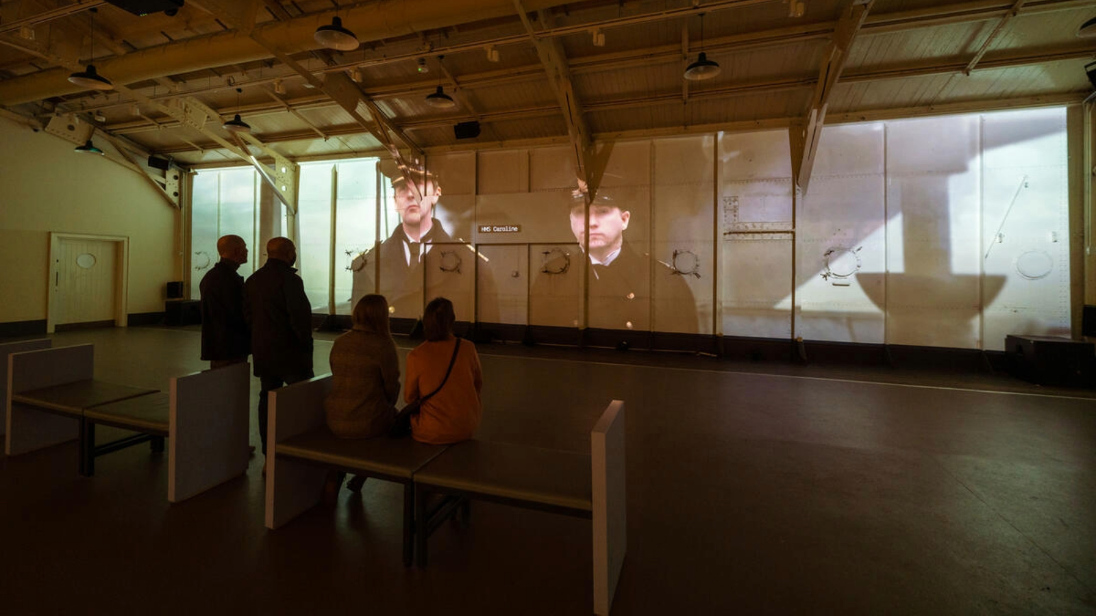 Visitors watching a projected film inside the Drill Hall of HMS Caroline in Belfast.
