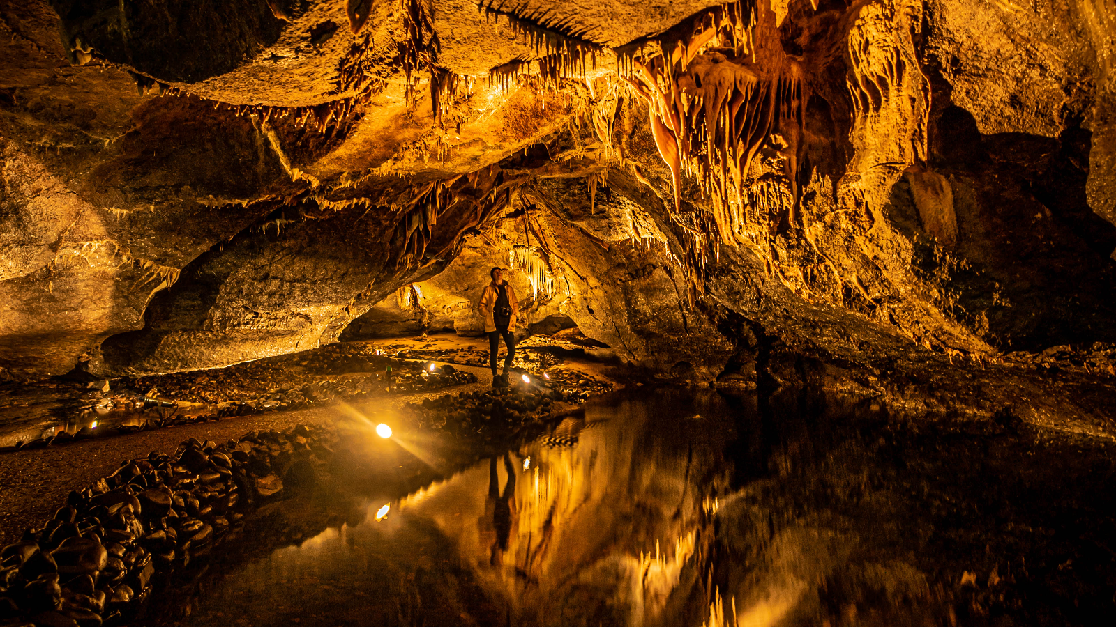 Visitor standing inside Marble Arch Caves surrounded by illuminated stalactites and reflective underground pools in County Fermanagh.