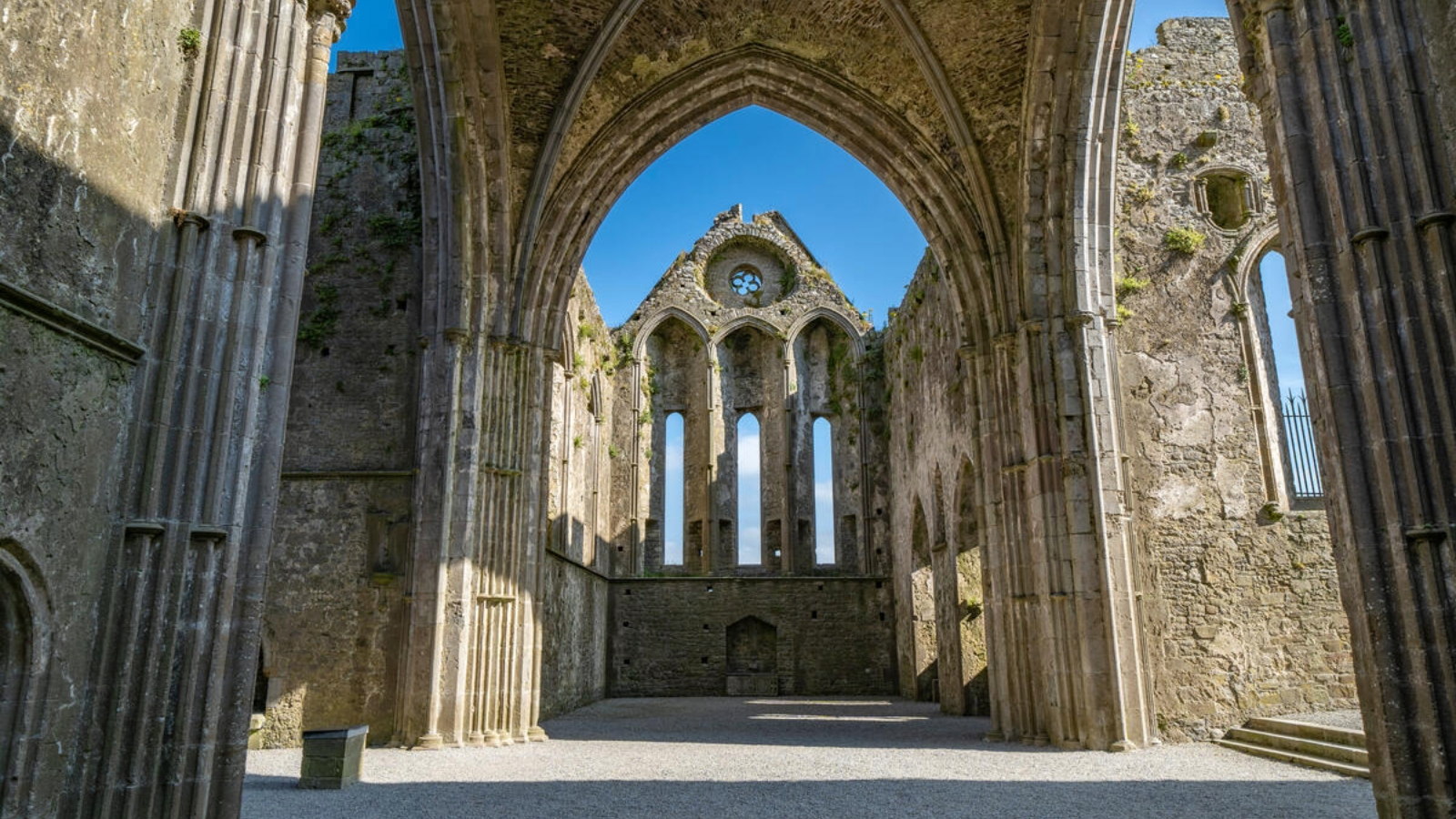 Inside the Rock of Cashel cathedral ruins, looking through a stone arch to tall Gothic windows.
