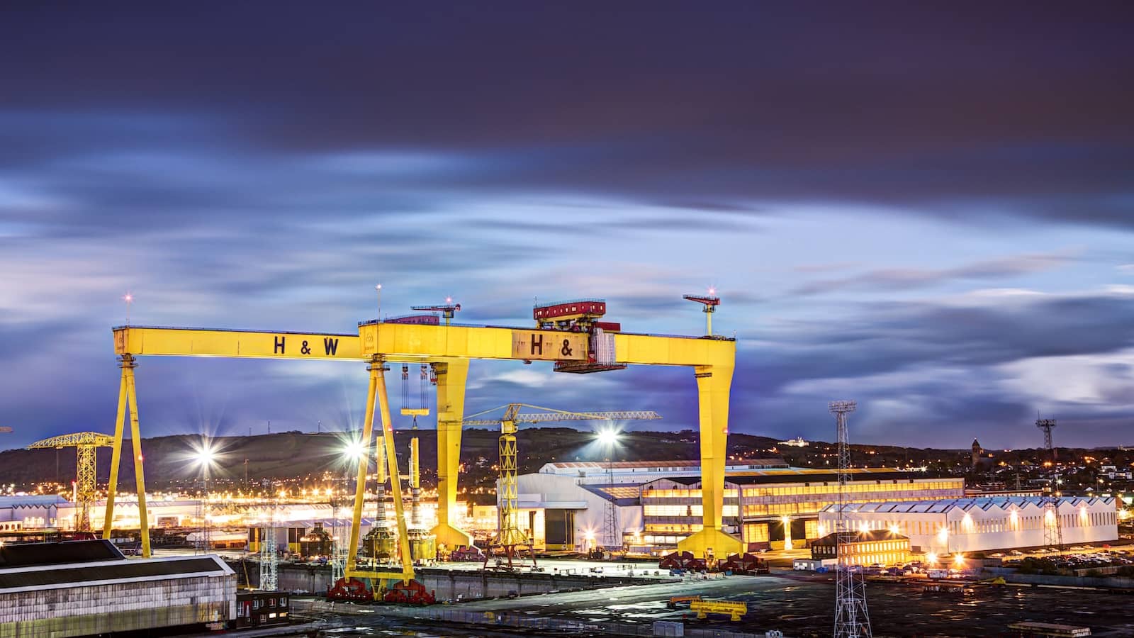 Harland & Wolff’s iconic yellow shipyard cranes lit up against a deep evening sky in Belfast.