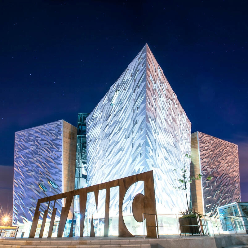 Titanic Belfast illuminated at night, with its angular silver façade and iconic Titanic sign in Belfast, County Antrim.