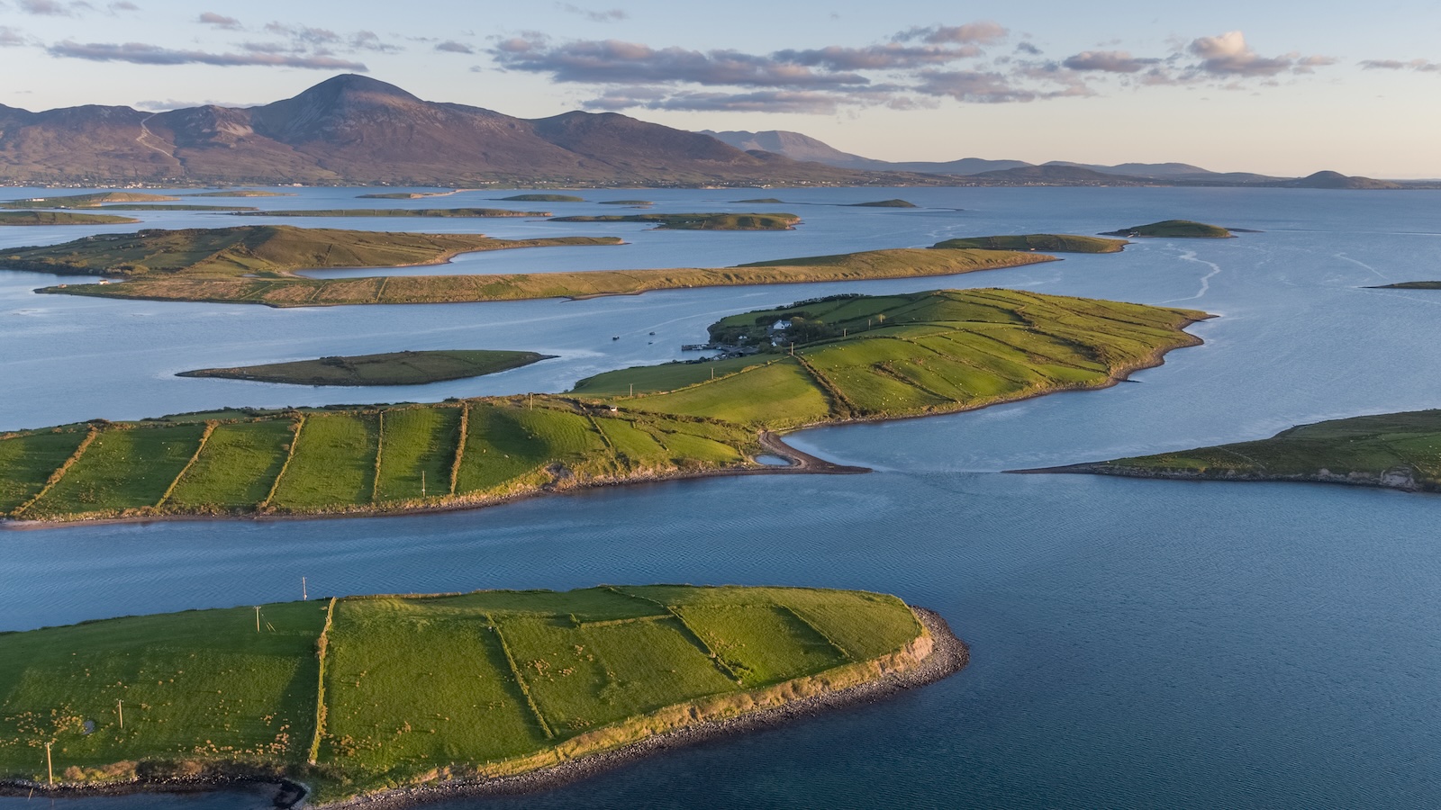 Aerial view of Clew Bay’s green islands with Croagh Patrick rising in the distance at sunset.