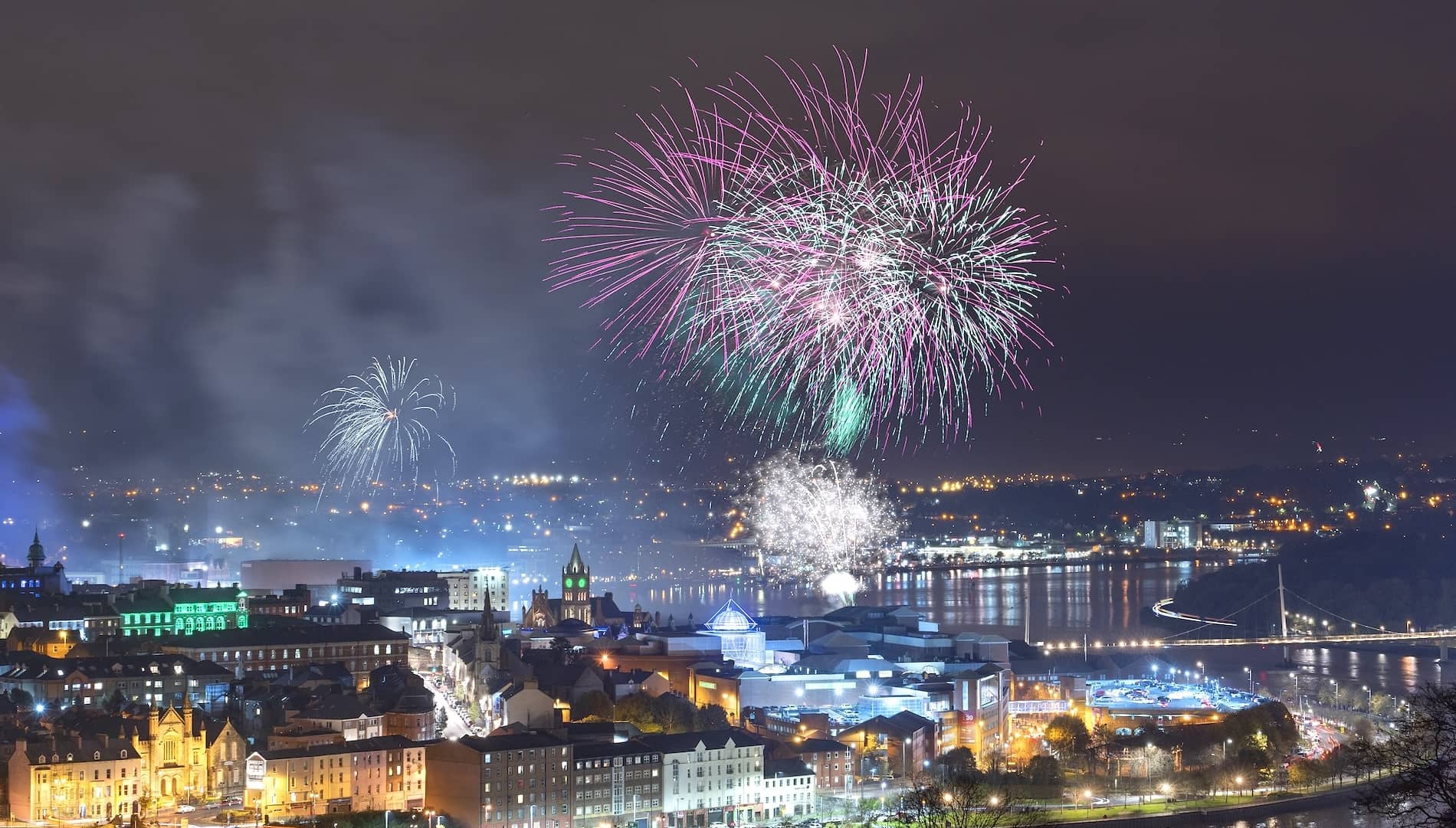 Vibrant fireworks explode over Derry~Londonderry city skyline at night during Halloween celebrations by the River Foyle.