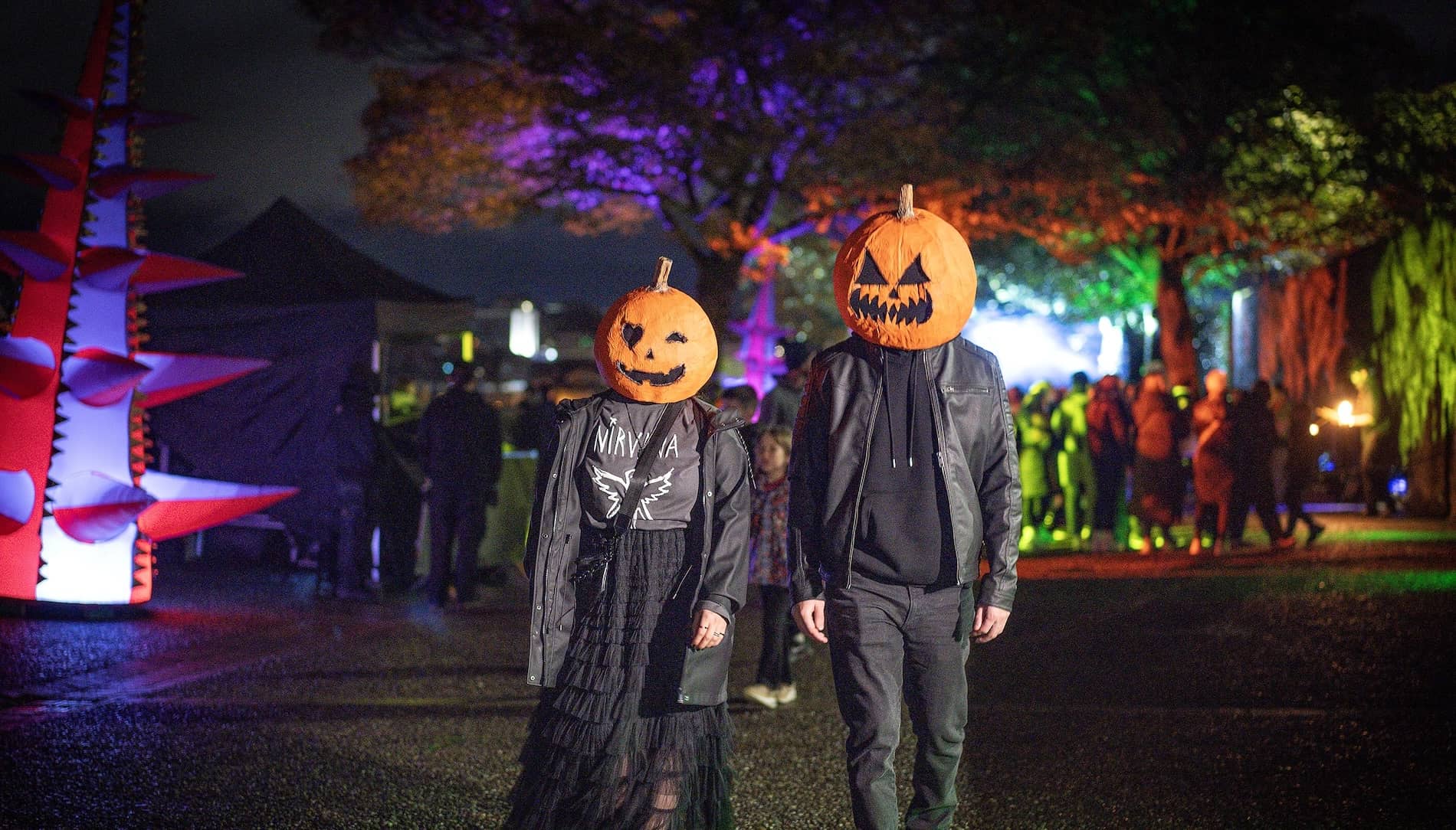 Two people with carved pumpkin masks walk through a Halloween festival in Derry~Londonderry.