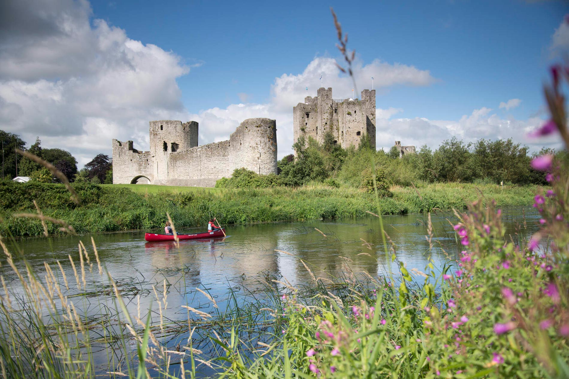 Medieval stone castle ruins with tall towers and walls reflected in a calm river in County Meath, Ireland.