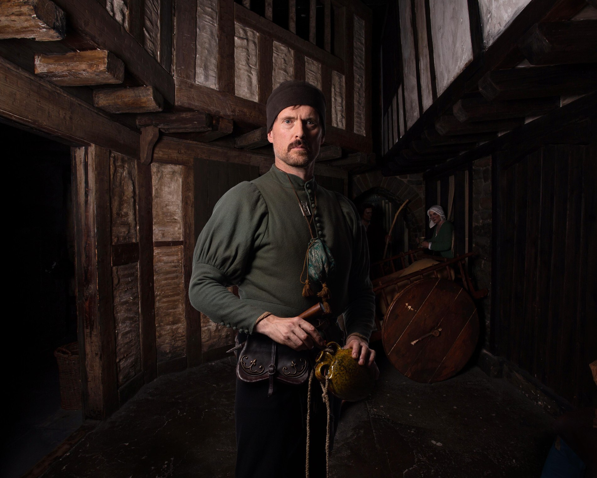 Man dressed as a Viking with green tunic and cap inside a recreated timber building in Ireland.