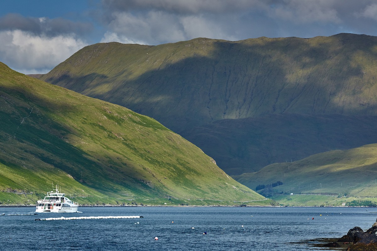 Tour boat on Killary Harbour in County Galway with green mountains rising steeply on either side under cloudy skies.