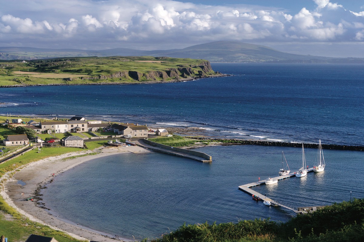 Small marina with yachts docked at Rathlin Island Harbour, Antrim, set beside curved beach and rugged coastal cliffs.