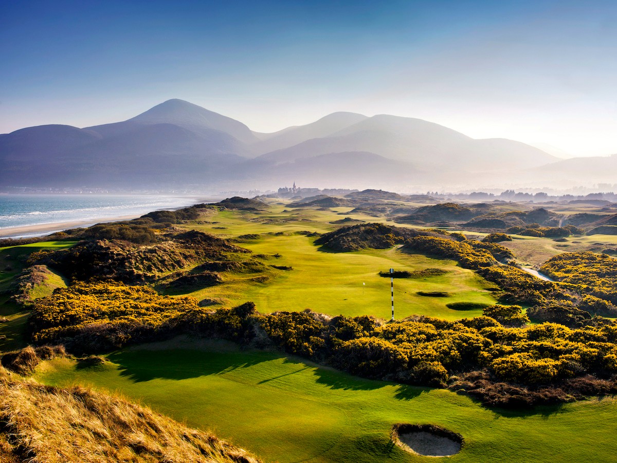 Expansive fairways of Royal County Down Golf Club with Mourne Mountains in the distance and coastline along the left.