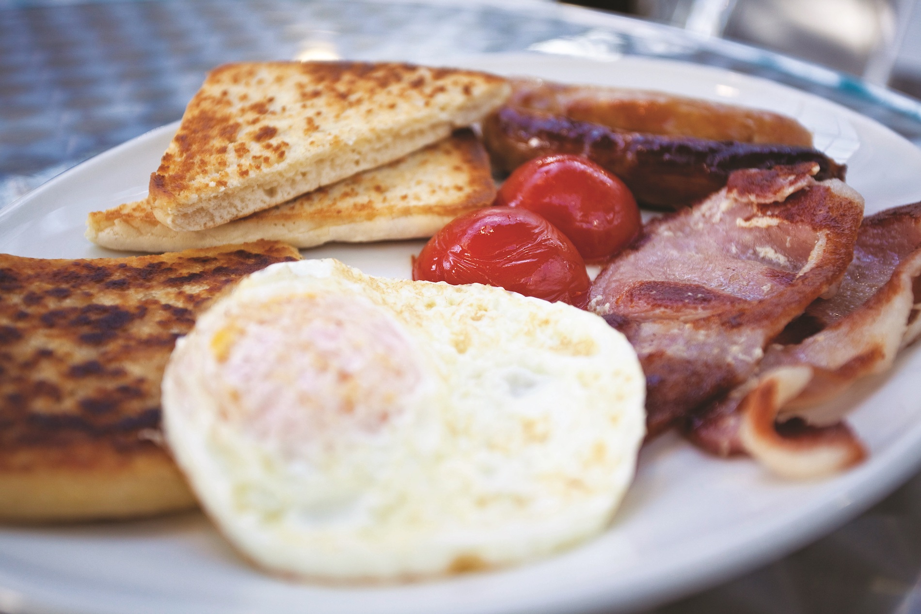 Plate of Ulster fry with fried egg, soda bread, bacon, sausage, and grilled tomatoes.