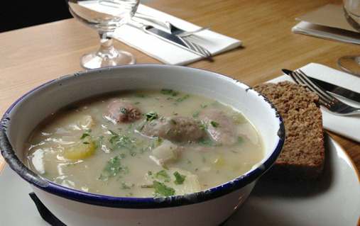 Bowl of hearty Dublin coddle stew with bread on the side at The Woollen Mills restaurant.