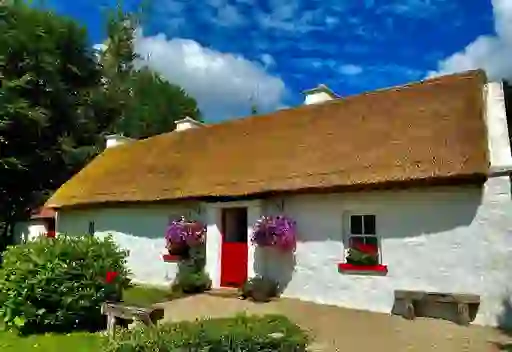 Traditional whitewashed thatched cottage with red trim and flower baskets in County Fermanagh.