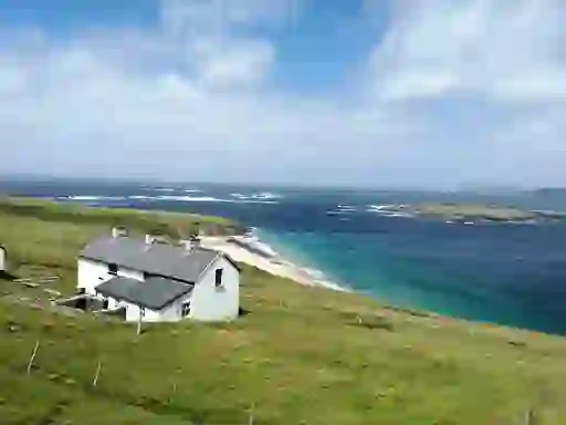 Remote white cottage overlooking a small beach and turquoise Atlantic waters on the Great Blasket Island, County Kerry.