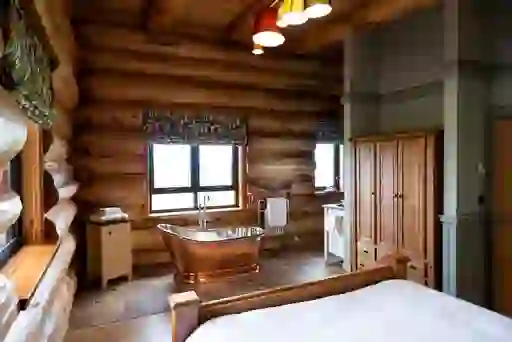 Rustic log cabin interior with a freestanding copper bath and woodland views in County Antrim.