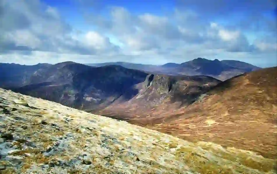 Rolling Mourne Mountains under blue skies with patchy clouds, seen from a frosty slope on a clear winter day.