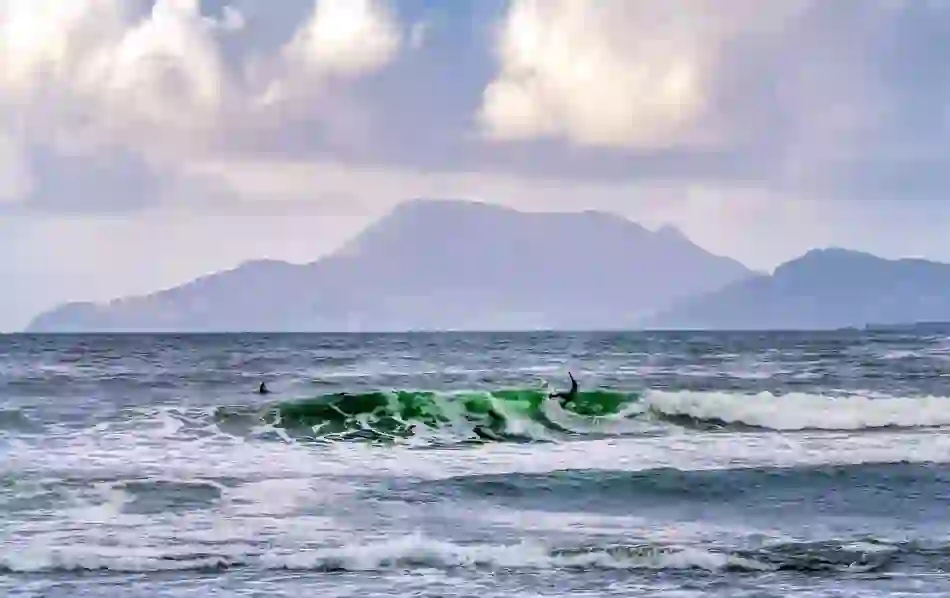 Surfer riding a wave at Tullan Strand, Bundoran, with misty mountains in the background and dramatic Atlantic swell.