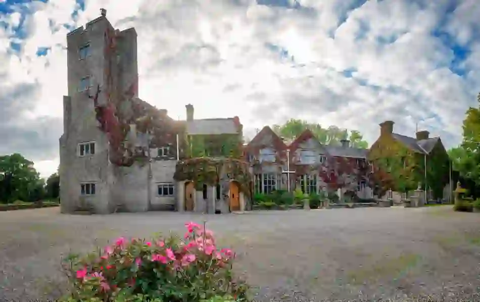Front entrance of Belle Isle Estate, County Fermanagh, draped in ivy with pink roses and gravel courtyard in foreground.