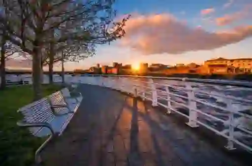 Sunset along Limerick’s riverfront with benches and view of King John’s Castle glowing under golden light.