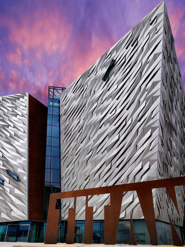 Striking Titanic Belfast museum with angular design lit by pink sunset sky in Northern Ireland.