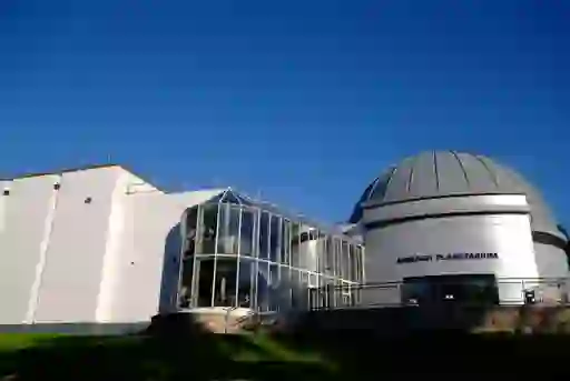 Exterior of Armagh Planetarium with domed roof and glass entrance lit by sunlight under a clear blue sky.
