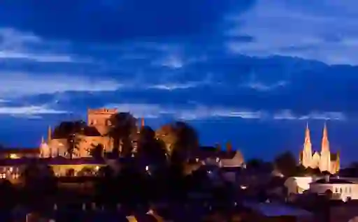 Armagh city skyline at dusk with both St Patrick’s Cathedrals illuminated under a deep blue sky above rooftops.