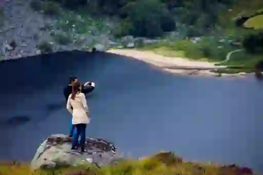 A couple stands on a rock overlooking Lough Tay in County Wicklow, taking in the scenic lakeside view.
