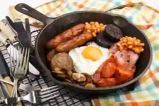 Traditional full Irish breakfast in a cast-iron pan with sausages, egg, and bacon.