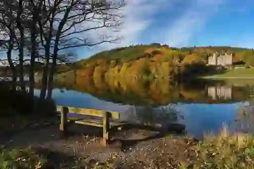 Bench overlooking Castlewellan Lake and Castle in County Down, surrounded by autumn trees and reflections.