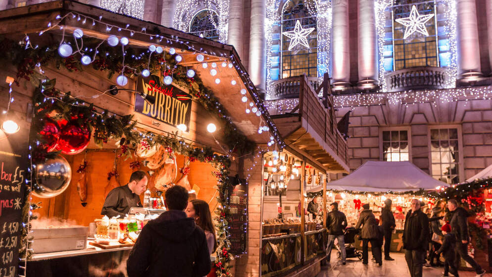 People browsing food and gift stalls at a Christmas market decorated with lights in Belfast