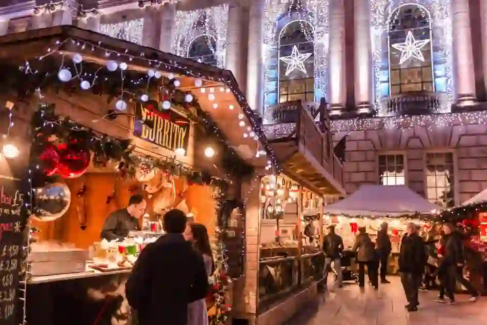 People browsing food and gift stalls at a Christmas market decorated with lights in Belfast