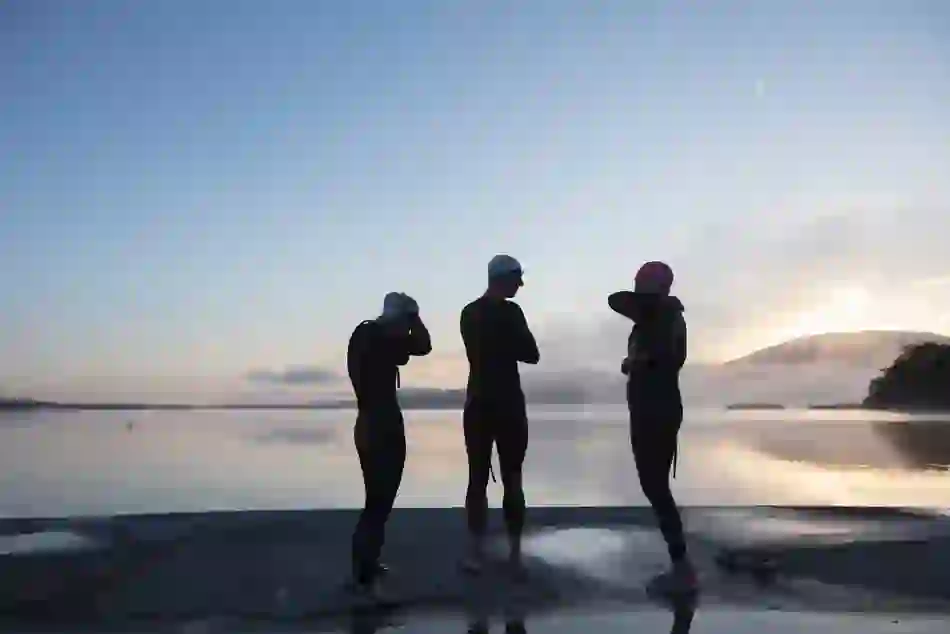 Swimmers in wetsuits prepare for a Christmas Day swim at dawn by a lake in Ireland.