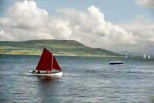 Traditional sailing boat with red sail crossing Donegal Bay beneath mountains on the horizon.