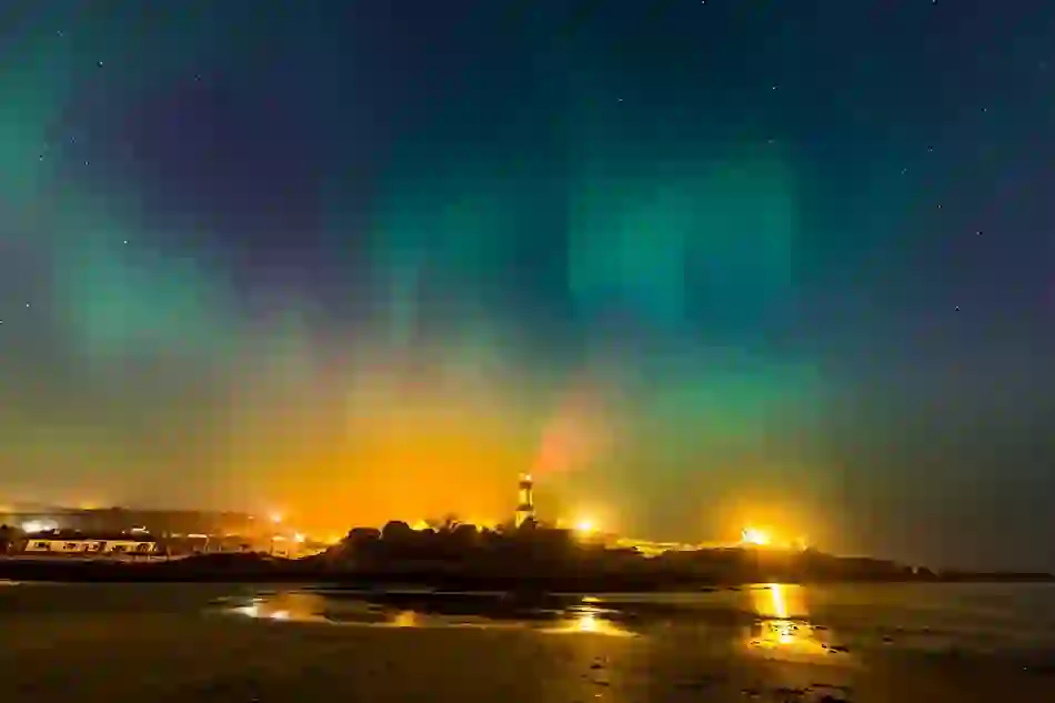 Aurora Borealis above Fanad Head Lighthouse with its light beam cast across the Atlantic Ocean.
